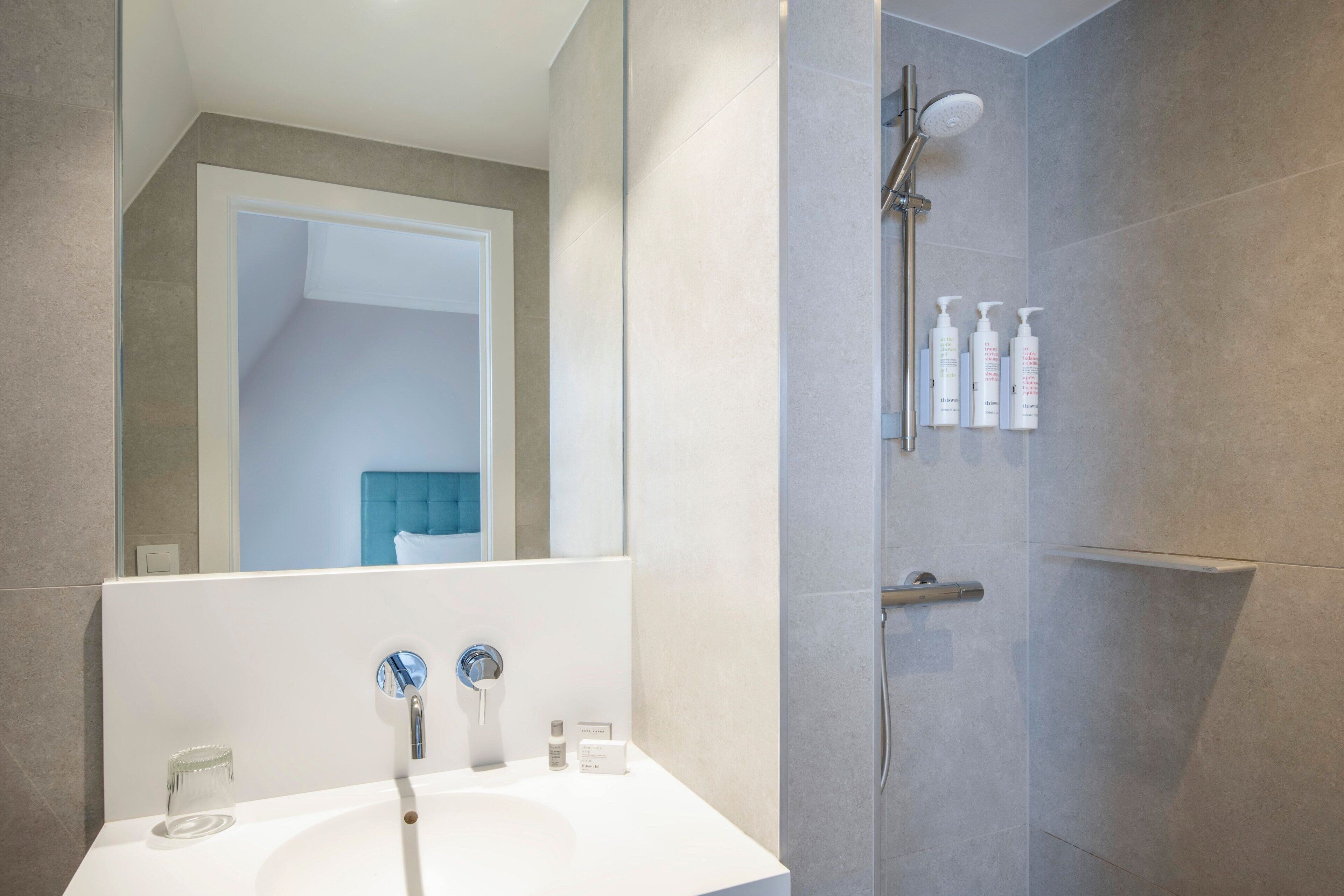 A modern bathroom with a white sink, a mirror, and a shower with a handheld showerhead.