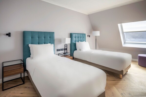 Una habitación de hotel con dos camas, una mesita de noche, una lámpara y una ventana.
