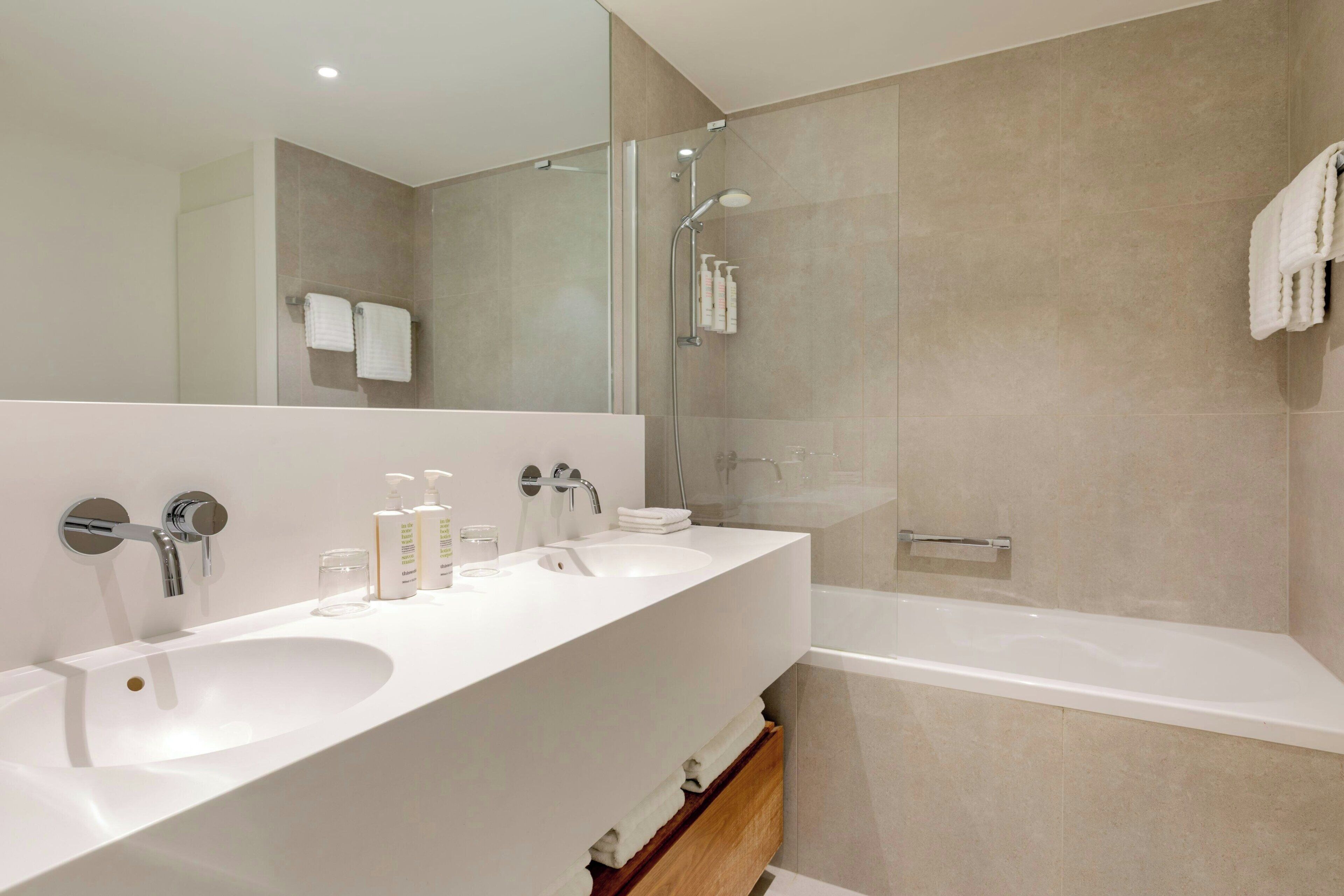 Un baño moderno con un espejo grande, dos lavamanos, ducha y bañera.