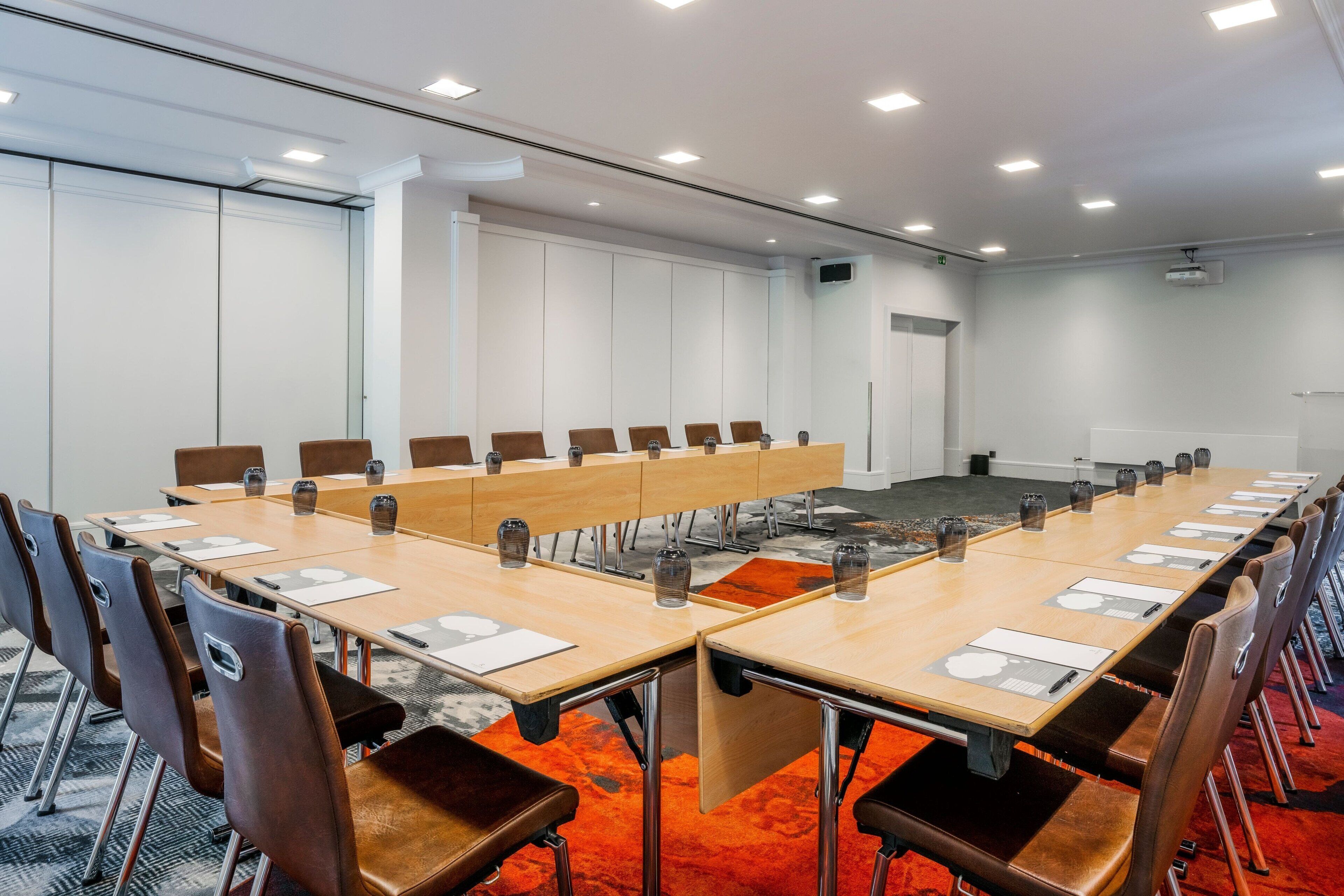 Ein Konferenzraum mit langem Tisch, mehreren Stühlen und Teppichboden.
