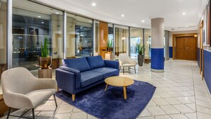 A modern lobby with a blue sofa, a round coffee table, and a beige armchair. - Marriott Executive Apartments Millennium Court (Budapest)
