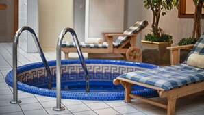 A small indoor pool with a blue mosaic design, a wooden lounge chair, and metal pool ladders. - Marriott Executive Apartments Millennium Court (Budapest)