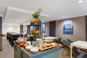 A hotel dining area with a buffet setup, including various food items and a potted plant on a shelf. - Marriott Executive Apartments Millennium Court (Budapest)