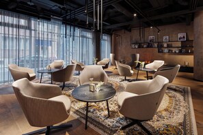 A modern lounge with multiple seating areas, a patterned rug, and a wall with framed pictures. - Mamaison Residence Downtown (Prague)