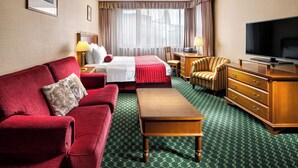 A hotel room with a bed, a red sofa, a wooden dresser, a television, and a desk with a lamp. - Mamaison Residence Downtown (Prague)