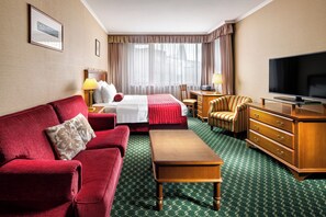A hotel room with a bed, a red sofa, a wooden dresser, a television, and a desk with a lamp. - Mamaison Residence Downtown (Prague)