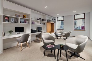 A modern office space with a white desk, multiple grey chairs, and a bookshelf filled with books. - Mamaison Residence Downtown (Prague)