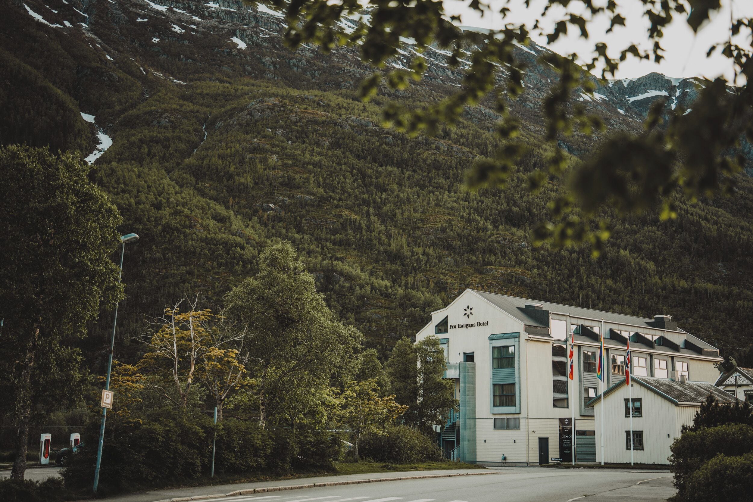 Un hôtel avec une vue sur les montagnes, un panneau indiquant l’emplacement du parking et une borne de recharge pour véhicules Tesla.