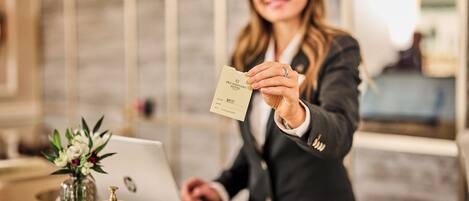 A person holding a card at a reception desk with a laptop, a vase with flowers, and a bell.