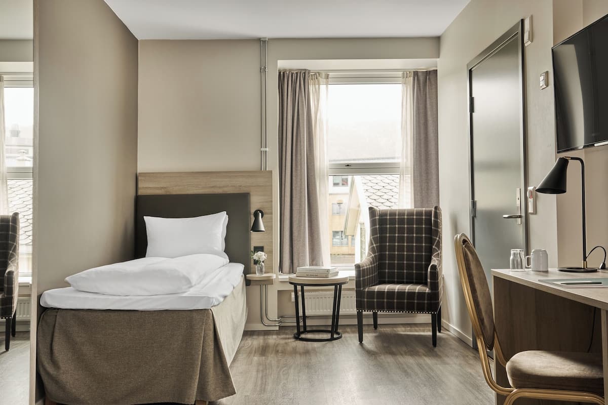 A hotel room with a bed, a desk, a chair, a TV, and a window with curtains.