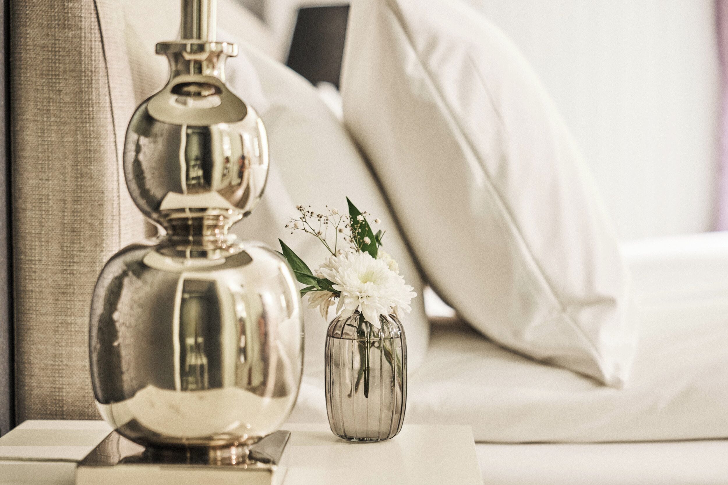 A bedside table with a metallic lamp and a small vase with flowers.