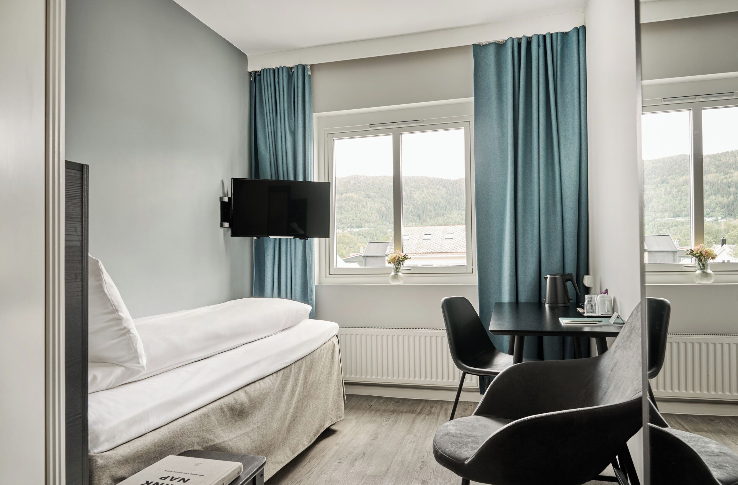 A room with a bed, a table with chairs, a TV, and a window with curtains.