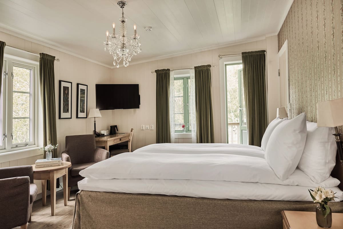 A hotel room with a large bed, a desk, a chair, a TV, and a chandelier.