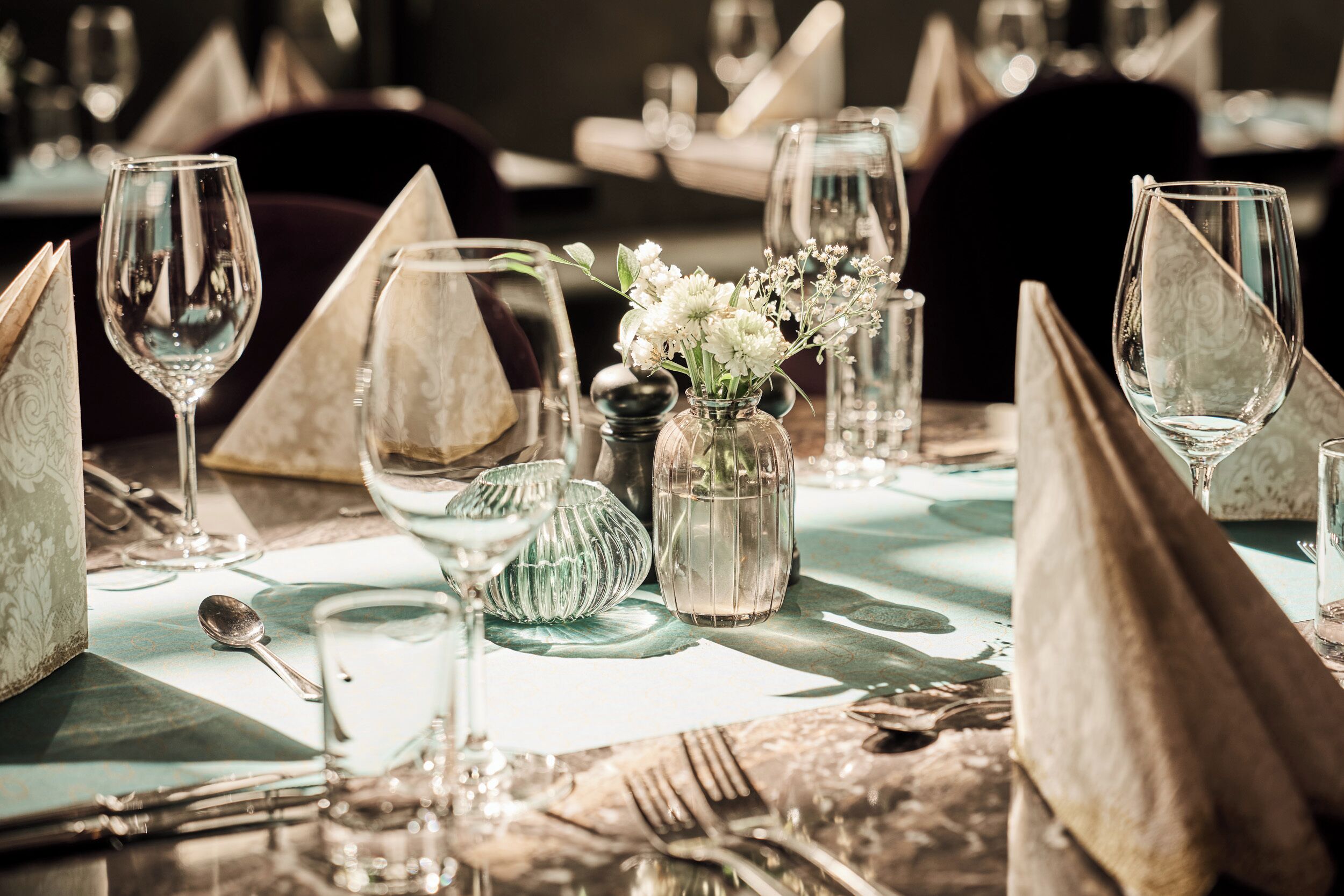 Une table dressée avec de la belle vaisselle, comprenant des verres à vin, une cuillère et un vase rempli de fleurs.