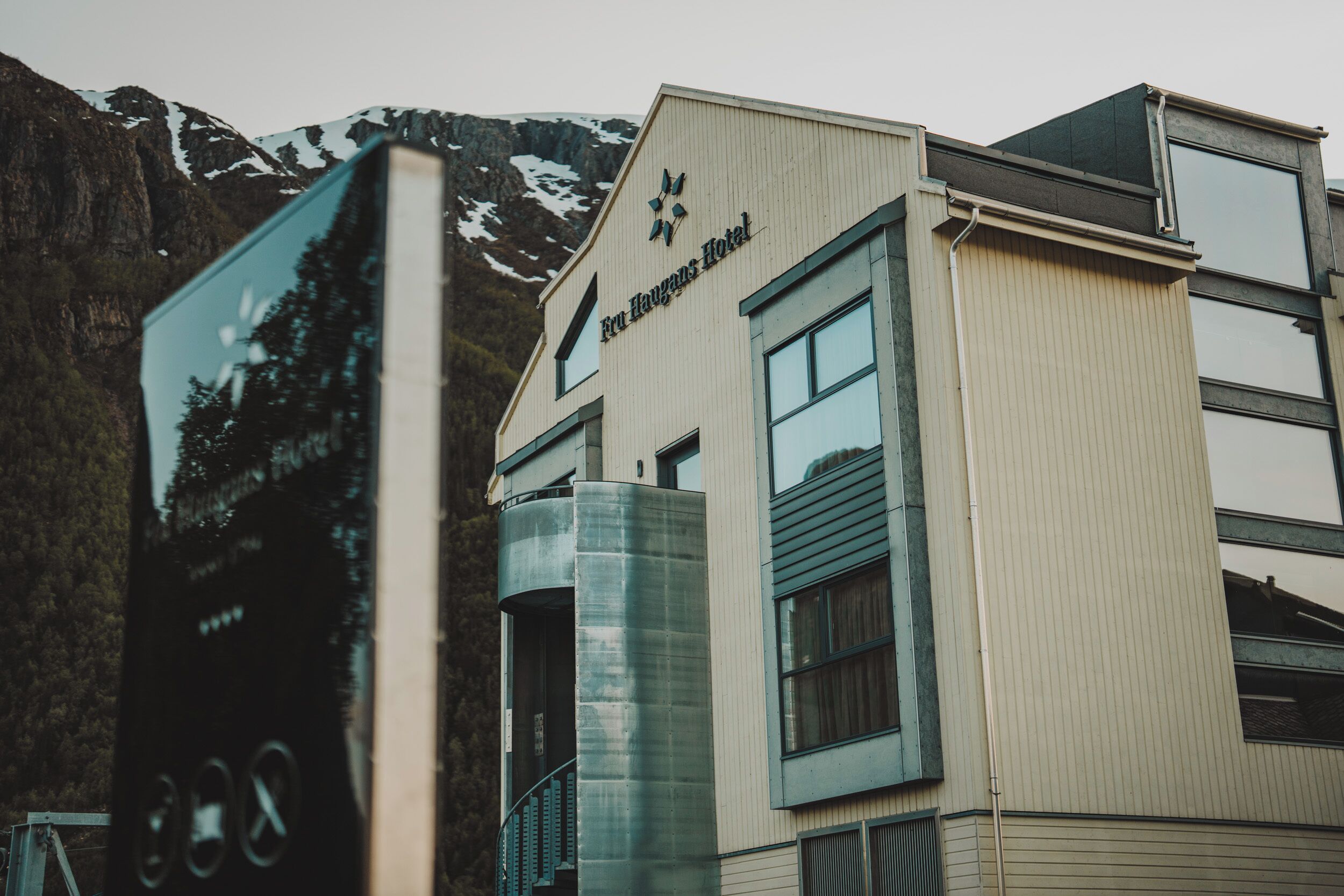 Un bâtiment sur lequel on peut lire l’inscription « Eur Høyas Hotel », et dont la façade en verre reflète des arbres et des montagnes.