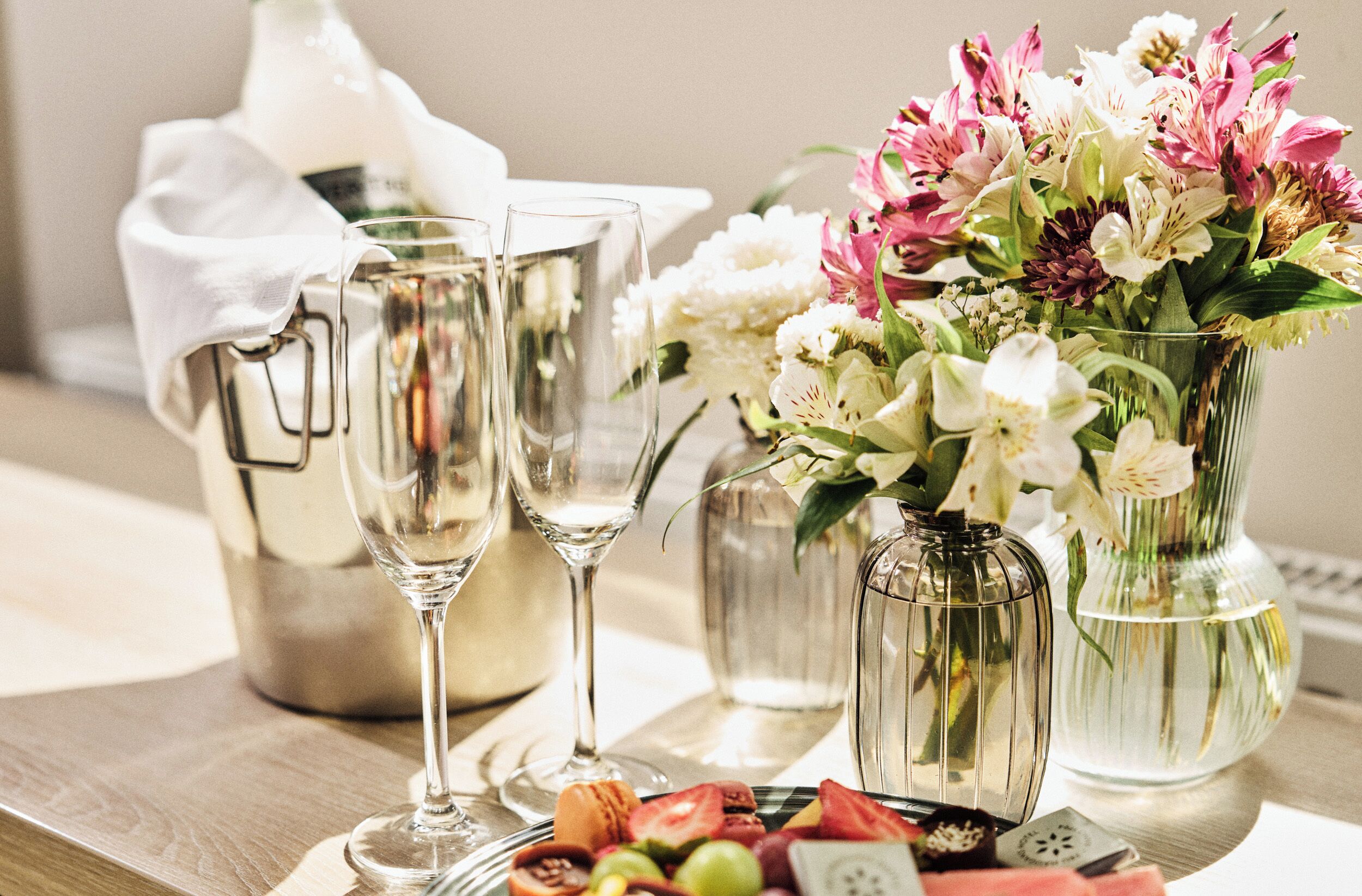 A table with a pitcher, glasses, a vase of flowers, and a fruit platter.