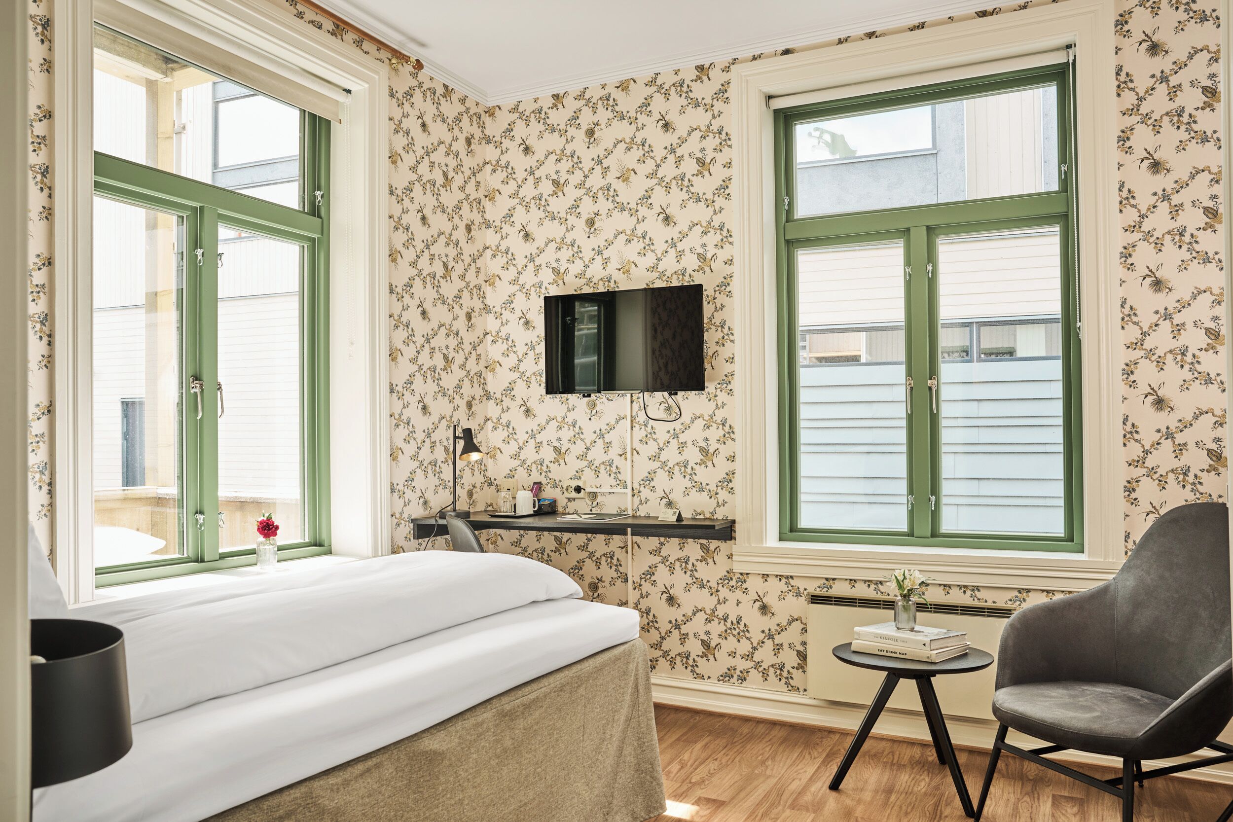 A bedroom with a bed, a desk, a chair, and two windows with green shutters.