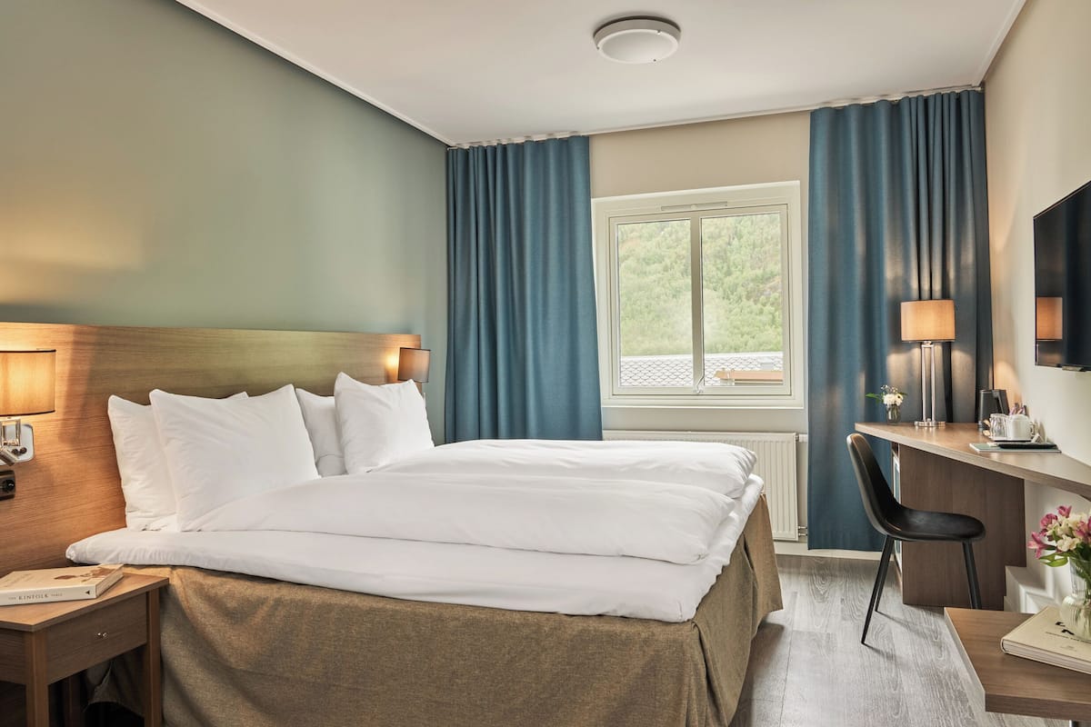 A hotel room with a bed, desk, chair, and a window with curtains.