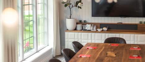 Een vergaderruimte met een lange houten tafel, stoelen, een potplant, een flatscreen-televisie en een buffet met diverse gerechten.