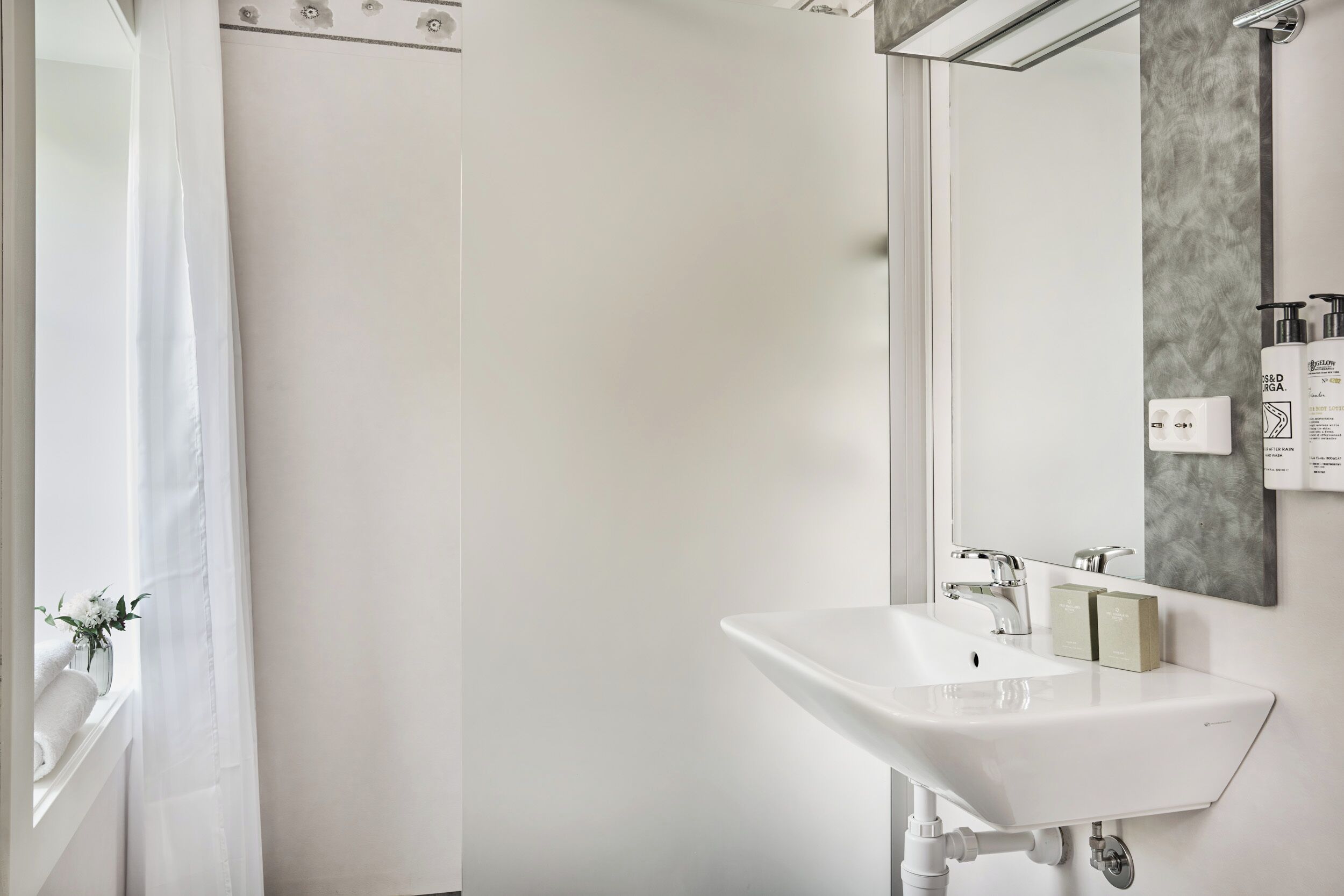 A modern bathroom with a white sink, a mirror, and a shower curtain.