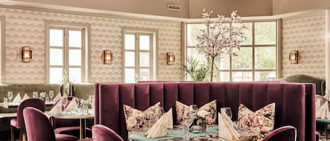 A dining area with plush seating, a chandelier, and patterned wallpaper.