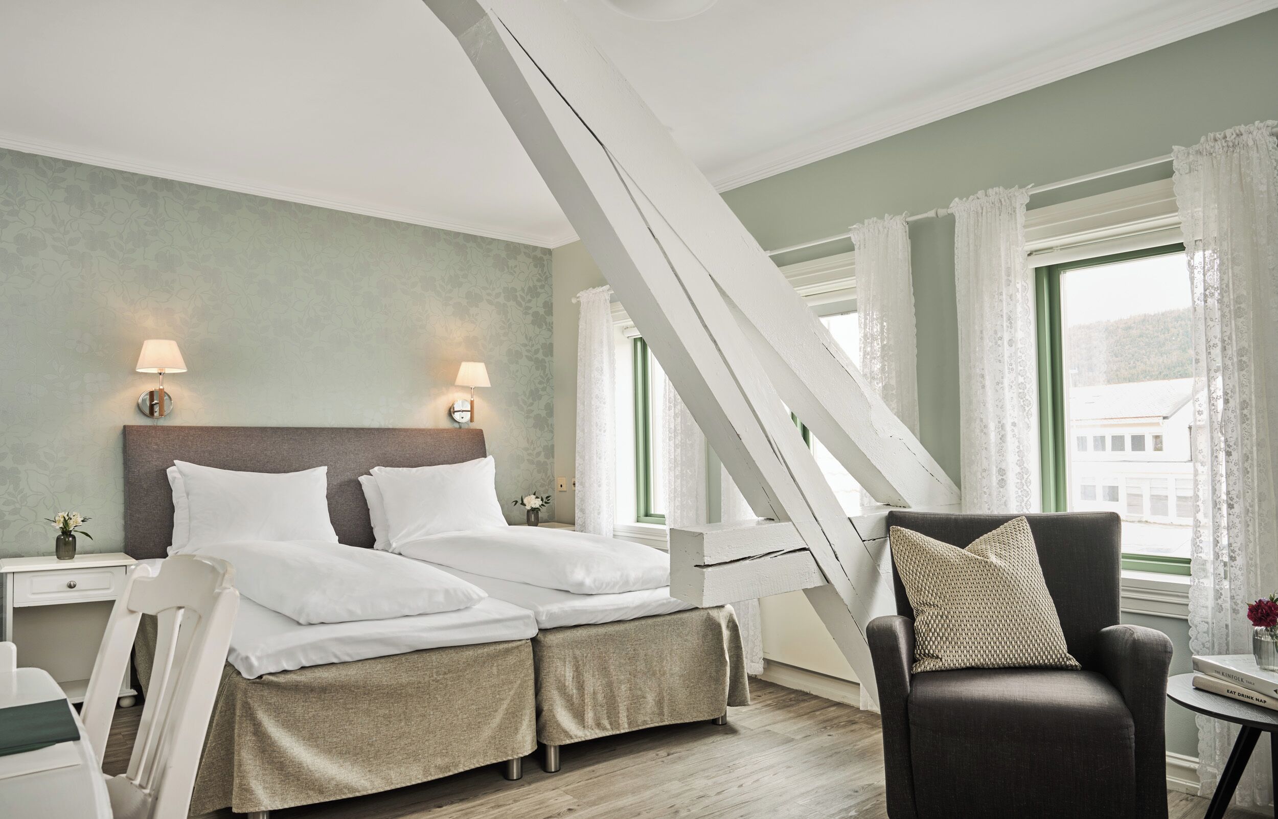 A hotel room with a bed, two bedside tables, a chair, and a window with curtains.