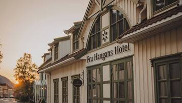 The exterior of the Fru Haugens Hotel with a classic architectural style, featuring large windows and a prominent sign.