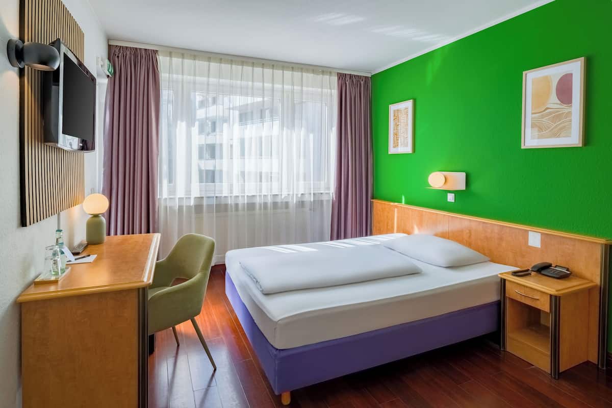 A hotel room with a bed, desk, chair, and a green accent wall.