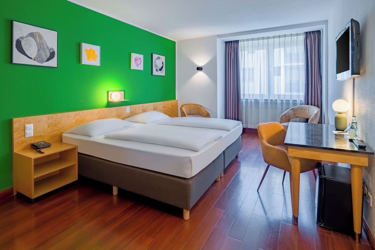 A hotel room with a bed, a desk, a chair, and a TV.
