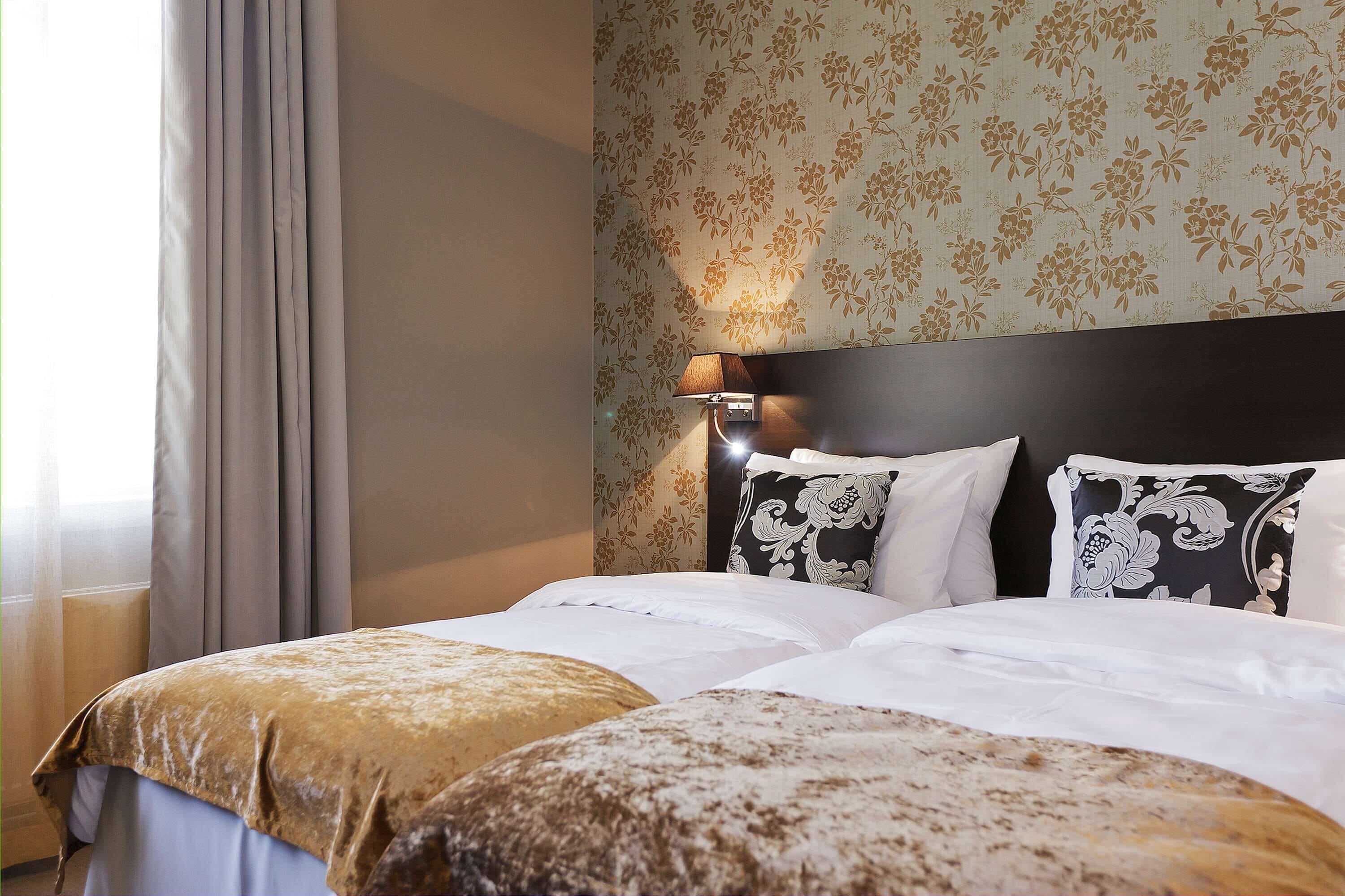 Een hotelkamer met een bed, nachtkastje, lamp en bloemenbehang.