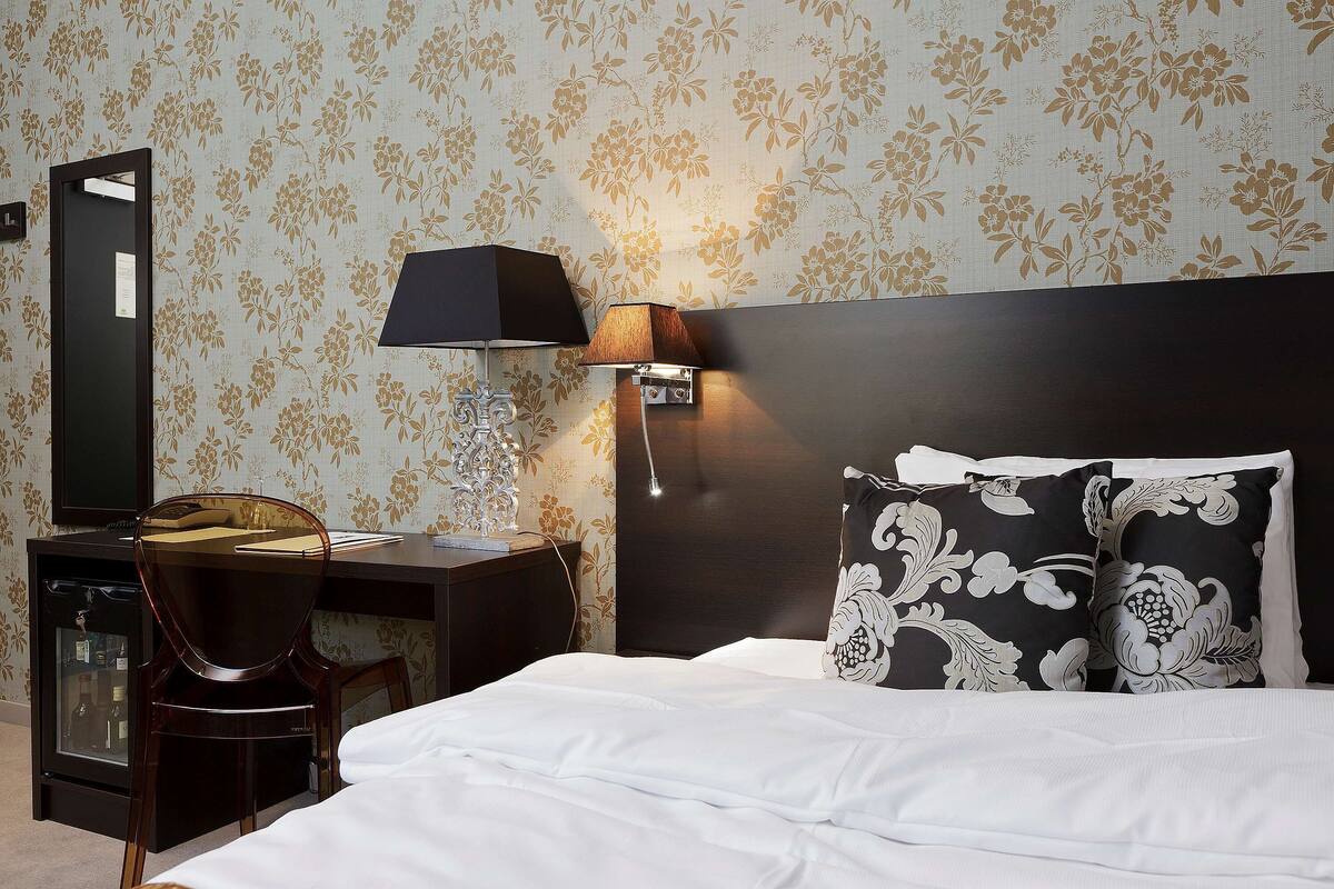 A hotel room with a bed, a desk, a chair, a lamp, and a mirror.