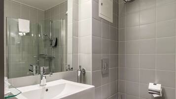 A modern bathroom with a large mirror, a white sink, a toilet, and a glass shower enclosure.