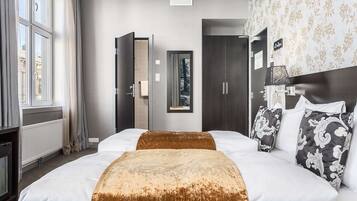 Een hotelkamer met een groot bed, een kaptafel, een raam met gordijnen, een radiator en een wandlamp.