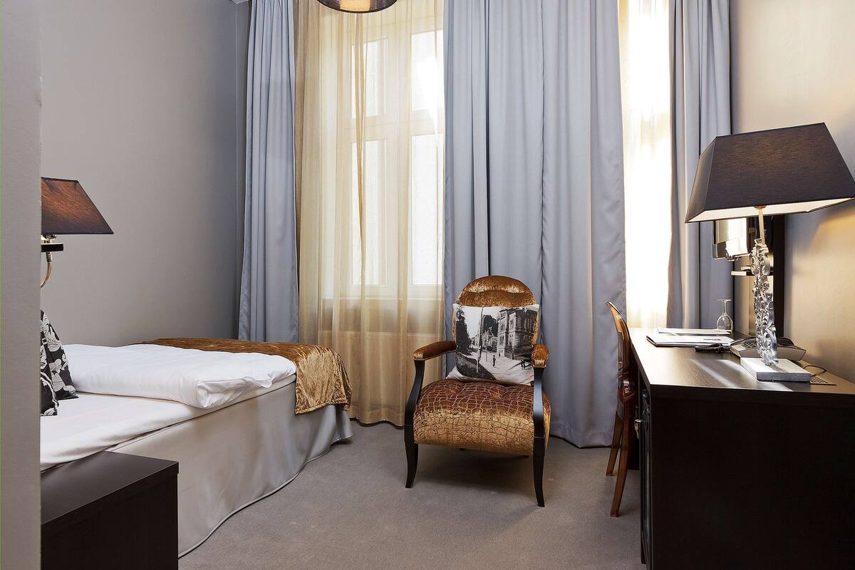 A hotel room with a bed, a chair, a desk, and a lamp.