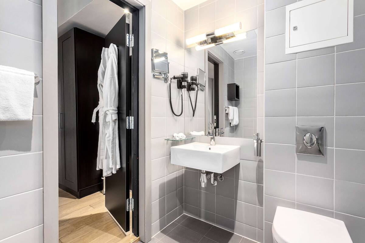 A modern bathroom with a white sink, a glass shower enclosure, and a dark wooden door.