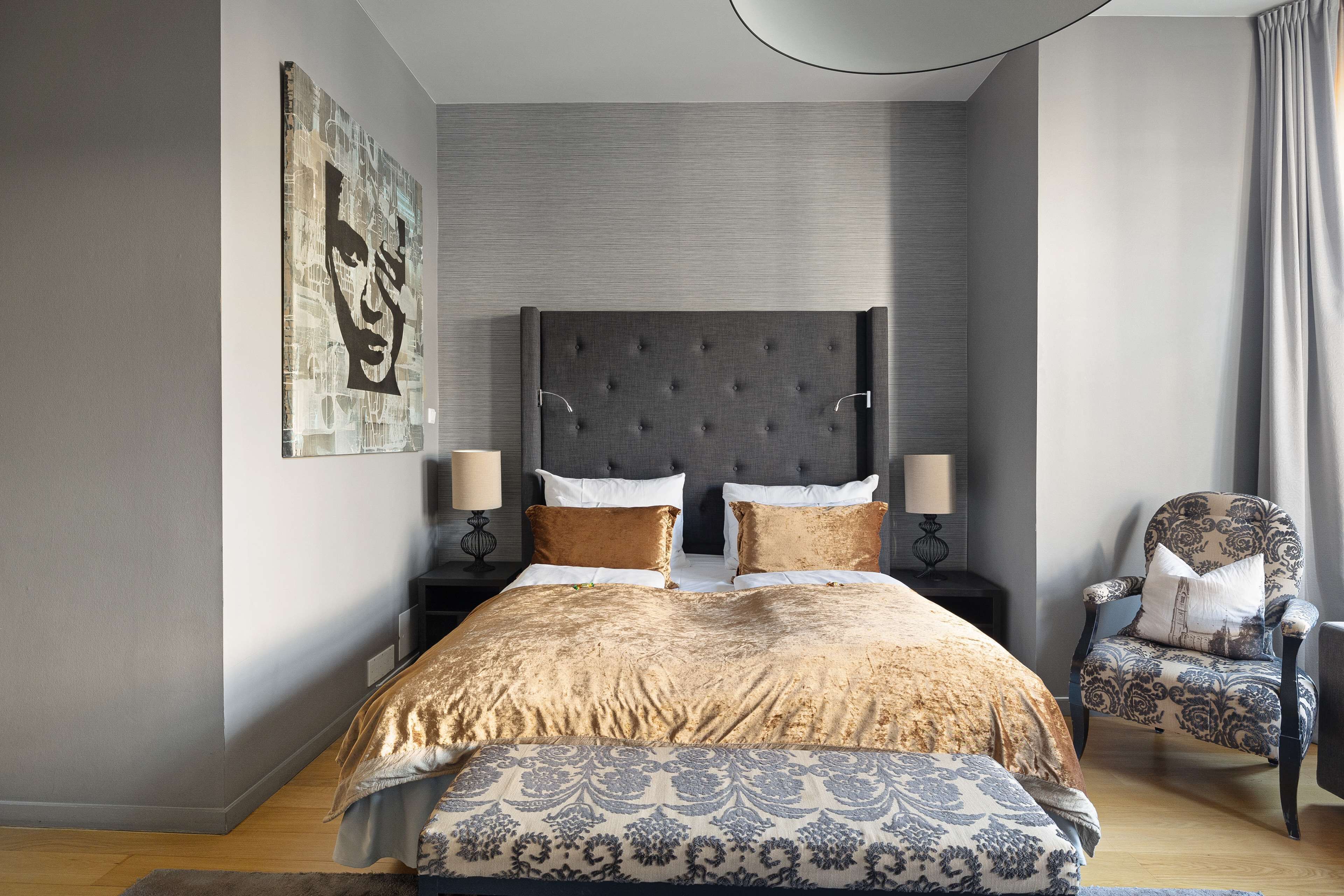 Een moderne slaapkamer met een groot bed, twee nachtkastjes, een stoel en een kunstwerk aan de muur.