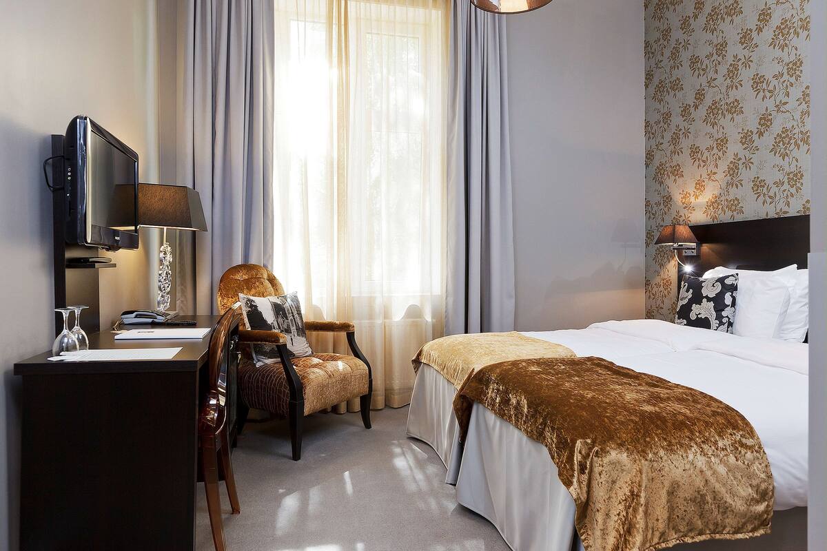 A hotel room with a bed, a desk with a television, a chair, and a lamp.