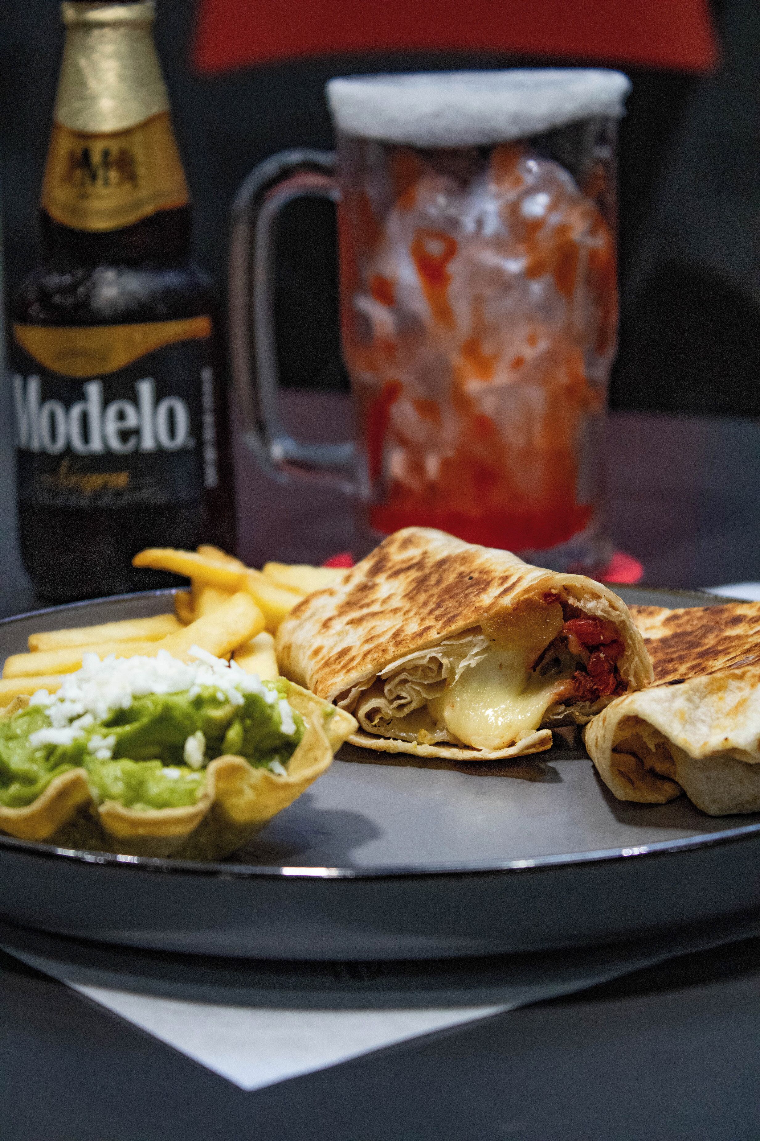 A meal with a burrito, guacamole, fries, and a Modelo beer bottle.