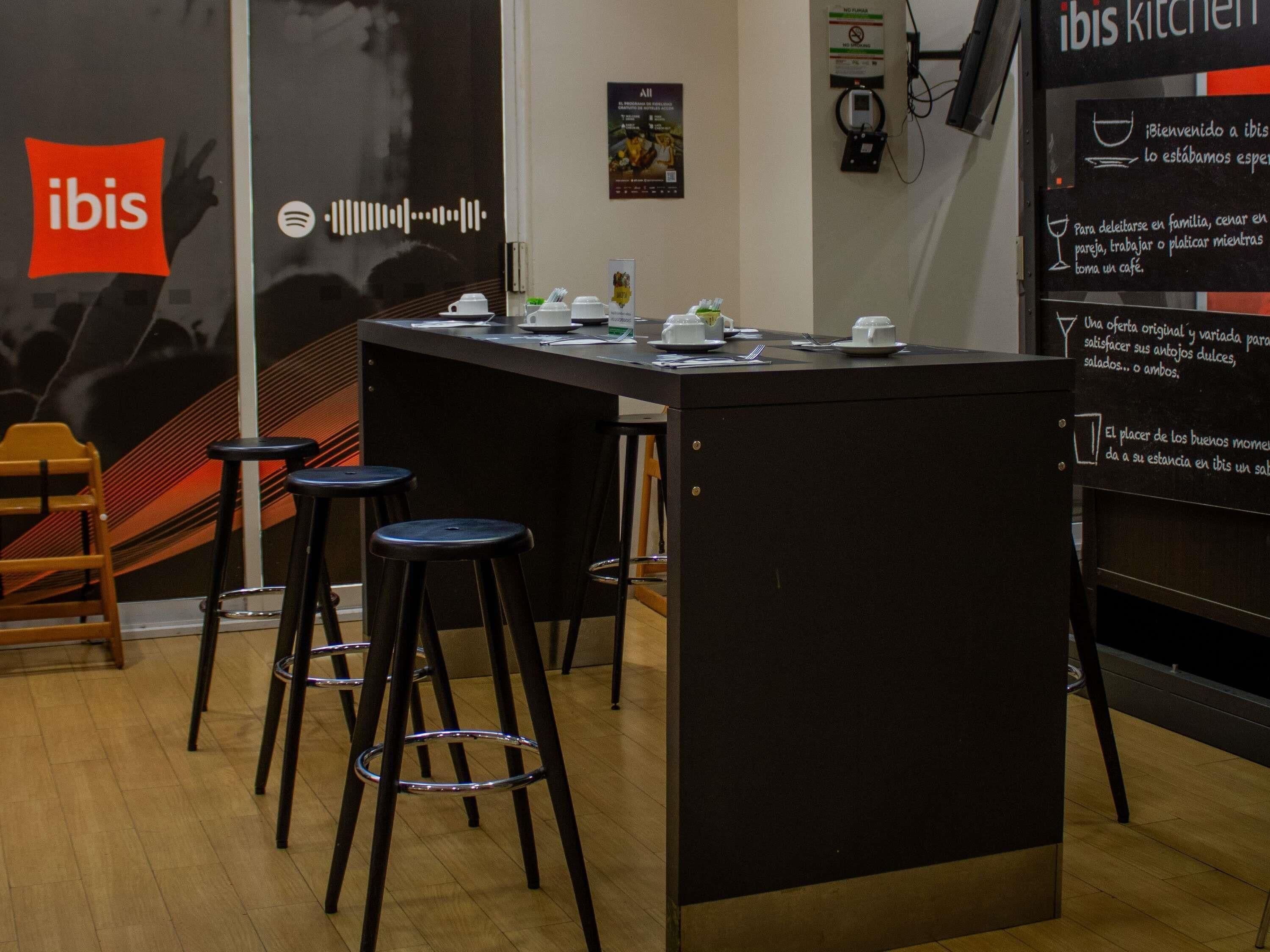 A kitchen area with a central island, stools, and a wall with a sign and a logo.