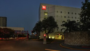 Un edificio moderno con un cartel llamativo de 'ibis', una entrada bien iluminada y un área de estacionamiento con una estructura roja.