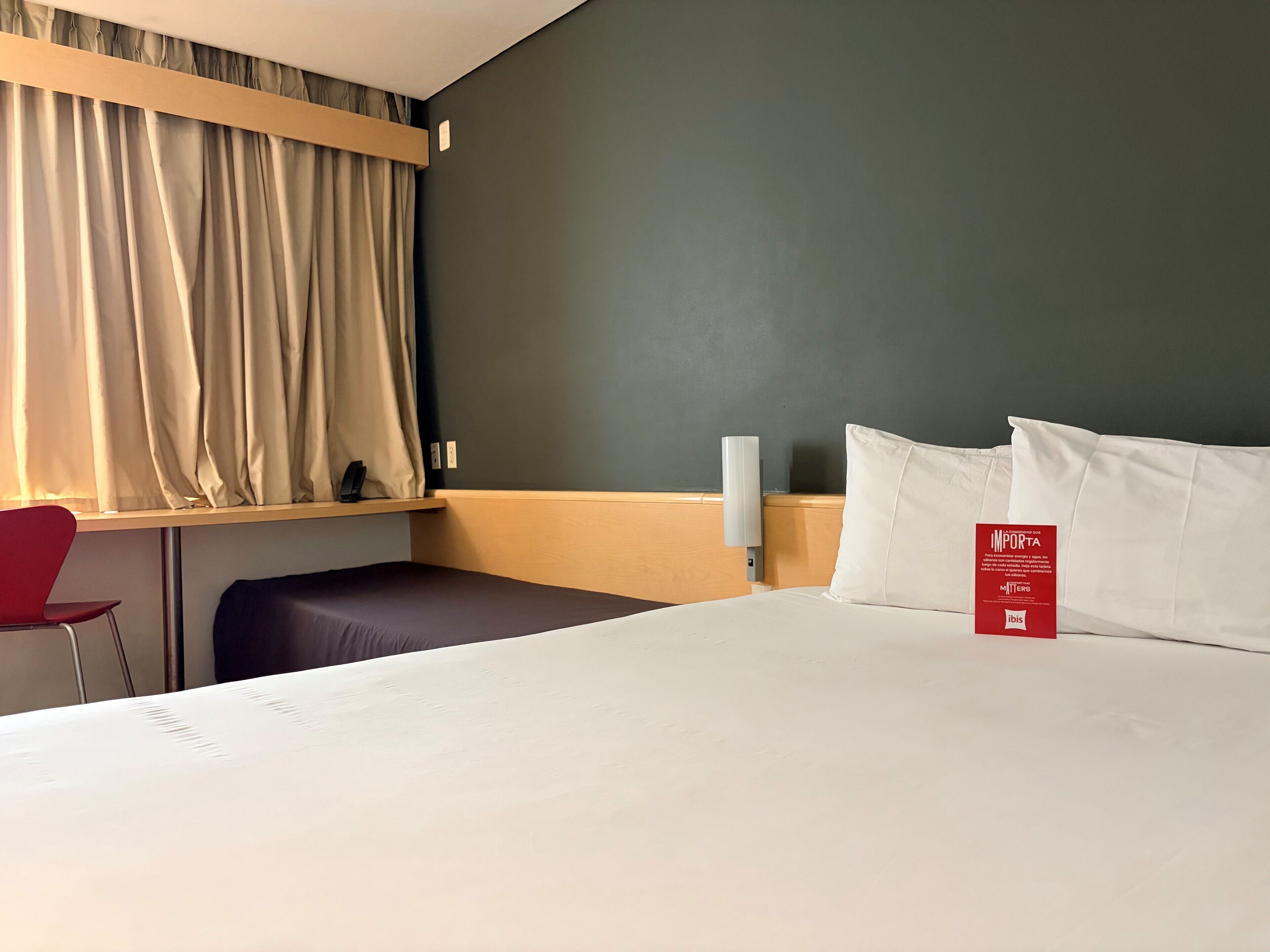 A hotel room with a bed, a desk, a chair, and a window with curtains.