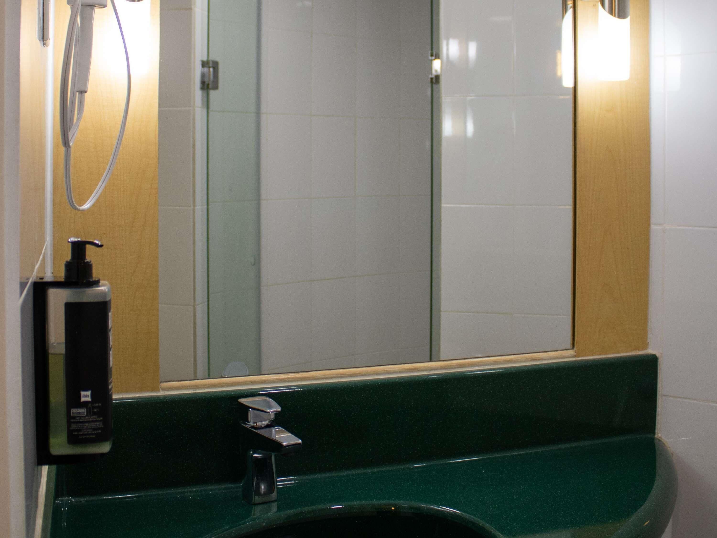 Un baño con un lavabo verde, un espejo, dispensador de jabón y ducha.