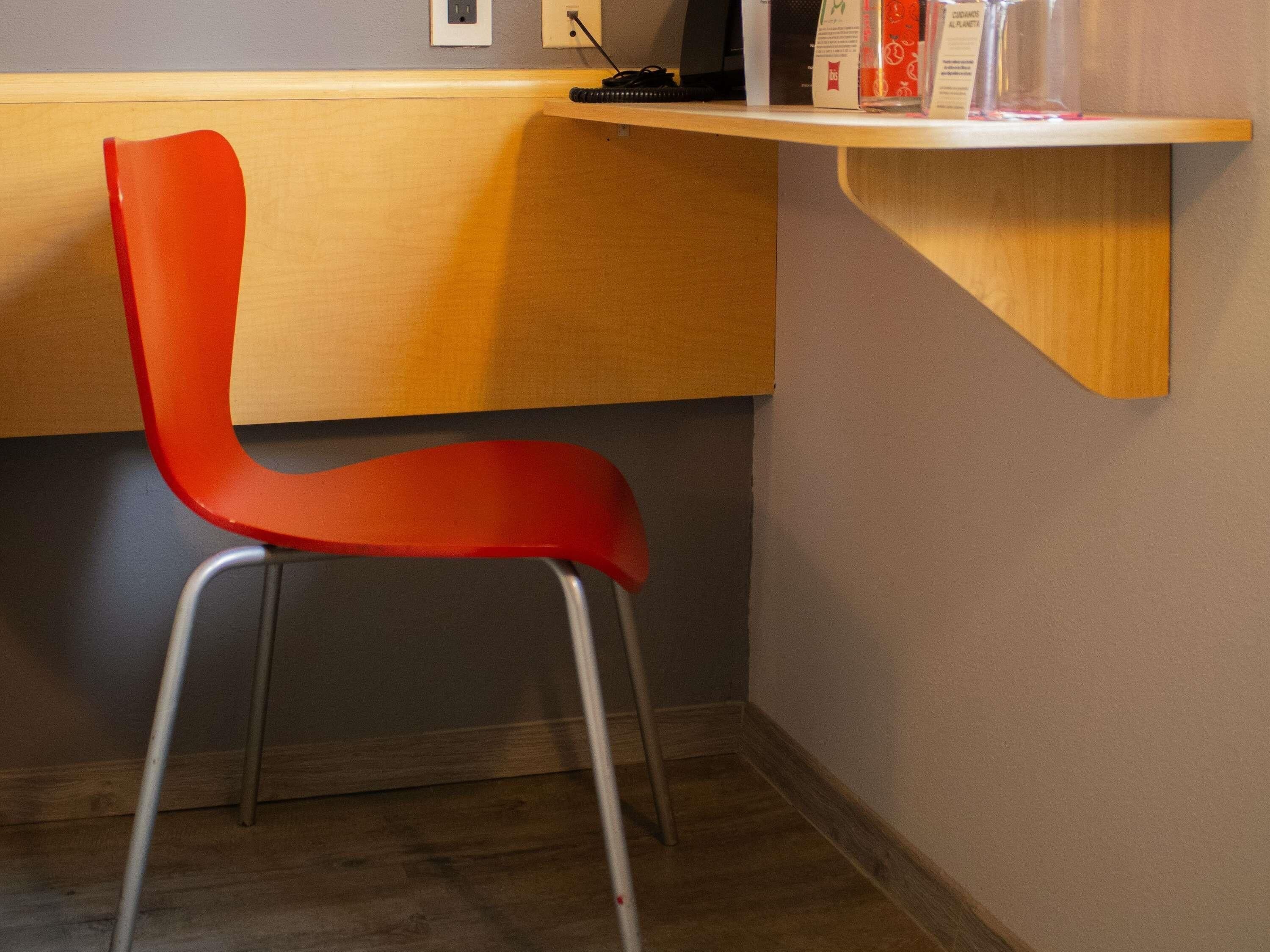 A red chair with metal legs, a wooden desk, and a shelf with items.