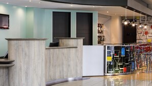 Ett modernt receptionsområde med en böjd receptionsdisk, ett vitrinskåp i glas med färgglada föremål och en bardisk med hängande pendellampor.