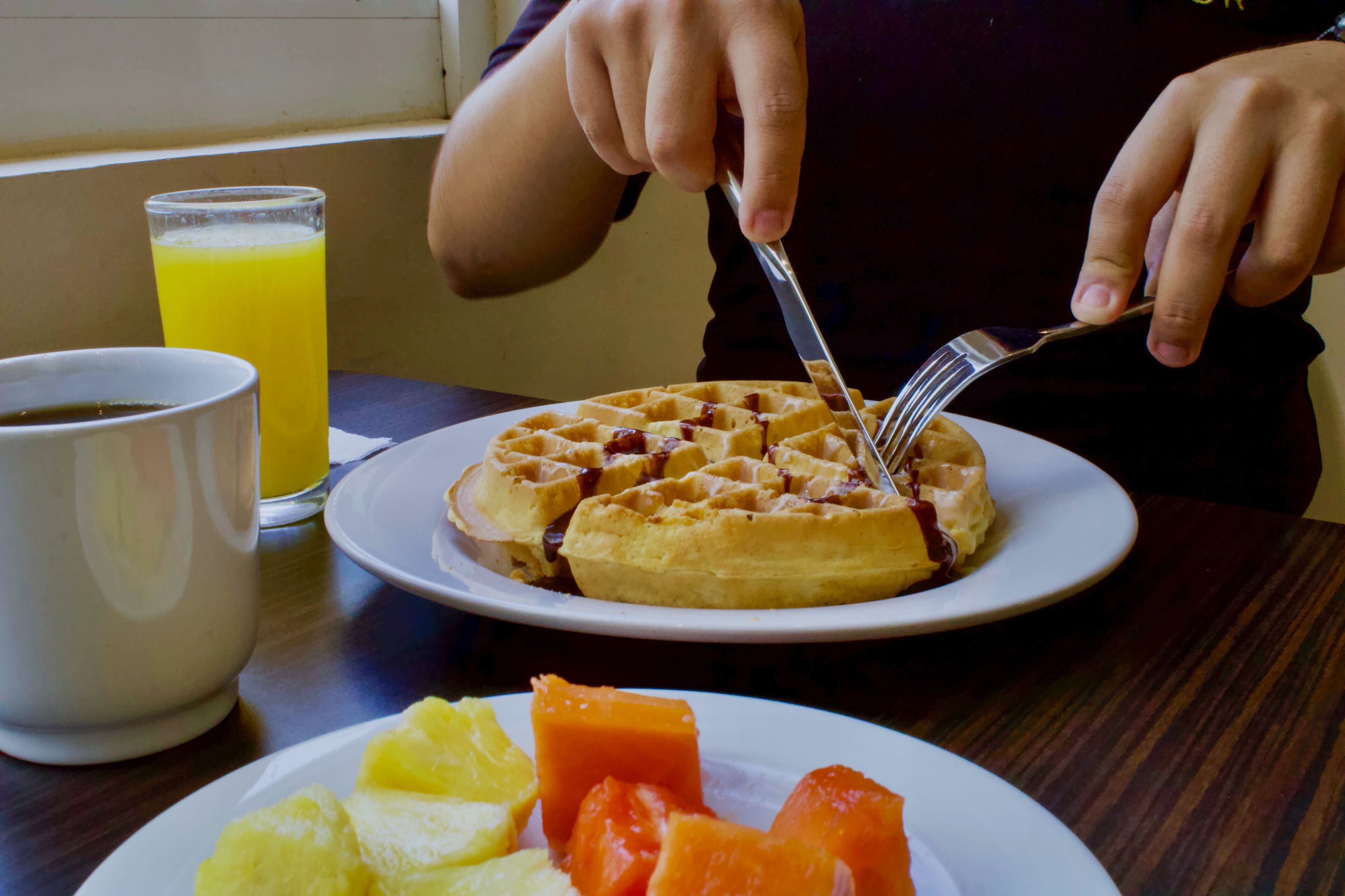A breakfast setting with waffles, fruit, and a glass of orange juice on a table.