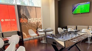 Un espacio interior moderno con mesa de fútbol, área de estar y una pantalla grande mostrando un evento deportivo.