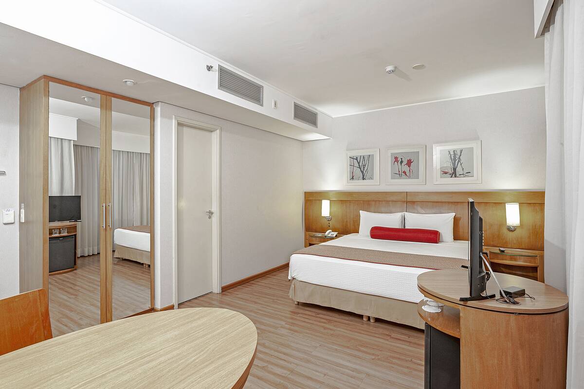 A hotel room with a bed, bedside table, desk, and a mirror.