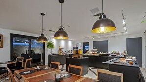 A modern kitchen with a central island, dining area with wooden tables and chairs, and pendant lighting. - SLAVIERO Moema (São Paulo)