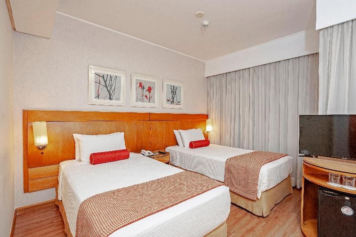 A hotel room with two beds, a television, and artwork on the wall.
