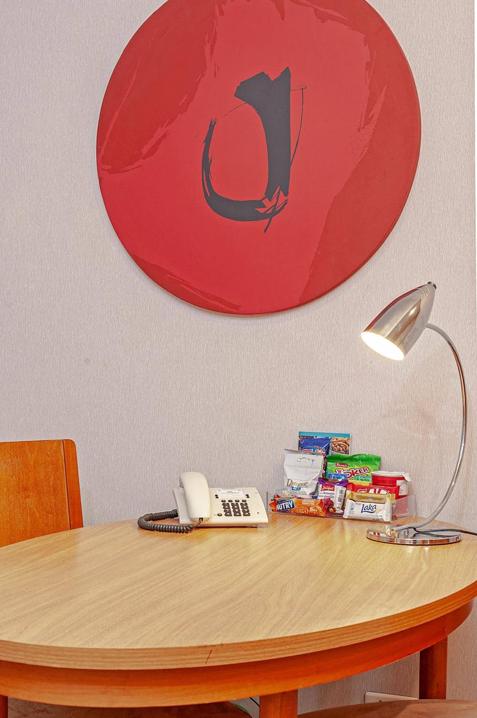 Ett runt träbord med en vit telefon, en lampa och olika sorters snacksförpackningar.